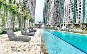 a swimming pool with chairs and palm trees and buildings at Stylish 2BR Near Food - Shops-Fast WiFi-Late Checkin in Gedong