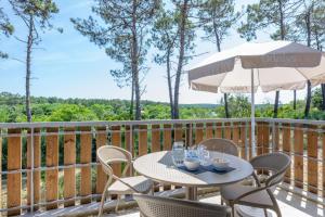 a table and chairs on a deck with an umbrella at Résidence Odalys Bleu Canopée in Mimizan +67 photos