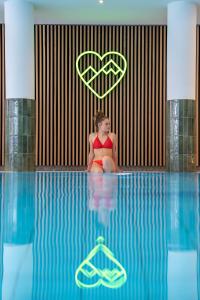 a woman in a red bikini sitting in a swimming pool at BERGlässig Hotel Bodenmais - 360 Grad Urlaub in Bodenmais