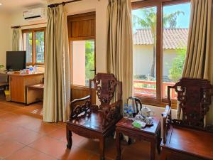 a living room with two chairs and a desk and windows at Sai Gon Can Gio Resort in Cần Giờ