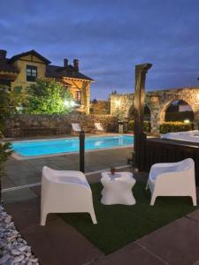 two white chairs and a pool in front of a house at Apartamentos la Leyenda in Santillana del Mar
