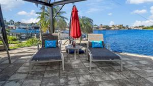 a patio with two chairs and a table with a red umbrella at Rosegarden - PoolSpa and perfect water view in Cape Coral +47 photos
