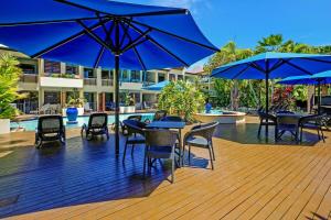a deck with tables and chairs with blue umbrellas at Chic Couples Retreat in Port Douglas
