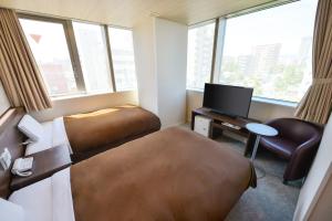 a hotel room with two beds and a desk and a tv at Hotel New Gaea Domemae in Fukuoka