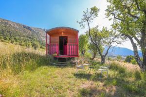 a red tiny house with a table and chairs in a field at Roulotte Ferme Saint-Pierre in Bargème