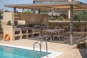 an outdoor kitchen and dining area with a swimming pool at Villa Portokalea in Maleme