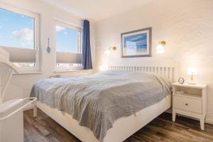 a white bedroom with a bed and two windows at Ferienwohnung Schmuckstück mit Meerblick Kronsgaard in Kronsgaard
