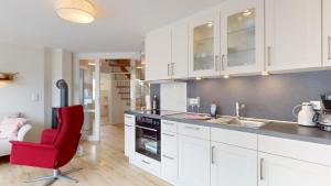a kitchen with white cabinets and a red chair at Haus Ostwind OSTWIND 'Bliedkupp' in Langeoog