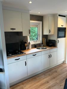 a kitchen with white cabinets and a sink at Chalet Aan de rand - Veluwe in Putten
