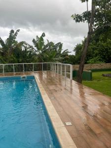 a pool with a wooden deck next to a fence at Suítes Sacai - Privacidade e Conforto in Conceição da Barra