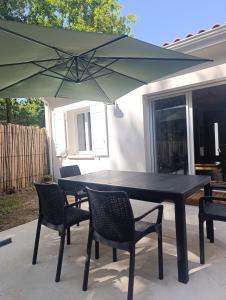 a black table and chairs with a green umbrella at Lisière Hébergements - Casa Mouette Mouette in La Tremblade