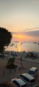 Mamdalis Private Rooms Stonetown في Ngambo: غروب الشمس على شاطئ مع سيارات متوقفة في موقف للسيارات