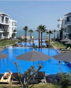 a swimming pool with umbrellas and chairs and the ocean at Appartement de luxe front de mer in Tamaris