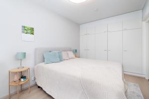 a white bedroom with a large bed and a table at Downtown Oulu 2BR, Sauna & Sea View Balcony in Oulu