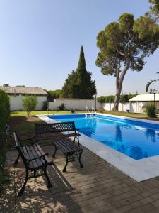 Dos bancos sentados junto a una piscina. en Casa rural Pinar de la Plata, en Arcos de la Frontera