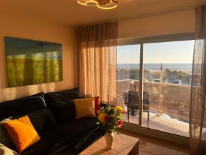 a living room with a black couch and a balcony at Le Paradis Fort Mahon, vue mer, élégance et fraîchement rénové in Fort-Mahon-Plage