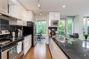 バンクーバーにあるSpacious Downtown Condo with Pool Gym & Parkingのキッチン(白いキャビネット、黒いカウンタートップ付)
