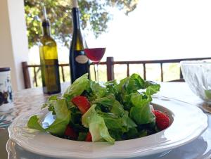 a bowl of salad with strawberries on a table with a bottle of wine at Catalina, ritorno al '70 tra mare e natura in Cannigione