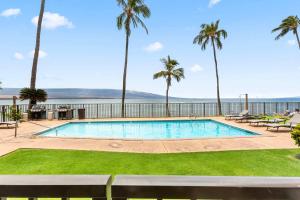 a swimming pool with palm trees and the ocean in the background at Lauloa 103 in Wailuku