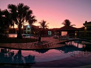 a pool with a table and palm trees at sunset at Búzios Beach Resort Apartamento Luxo Home Premium 2 in Búzios +13 photos