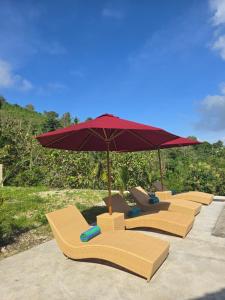 a row of lounge chairs with an umbrella at Dudu Cottage Nusa Penida in Nusa Penida +19 photos