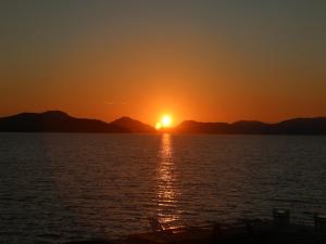 a sunset over the water with mountains in the background at Petrakis Beach in Lefkimmi