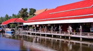 a building with a red roof next to a body of water at Greenfield Valley Fishing Resort in Hua Hin