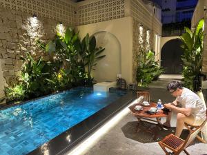 a man sitting at a table next to a swimming pool at 09 Villa in Can Tho