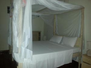 1 dormitorio con cama con dosel, sábanas y almohadas blancas en Kilimandogo Residence en Malindi