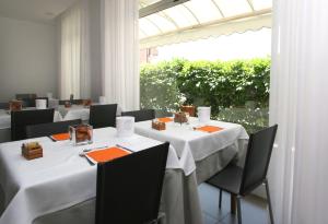 restauracja z białymi stołami i krzesłami oraz dużym oknem w obiekcie Hotel Simi Lan w Lignano Sabbiadoro