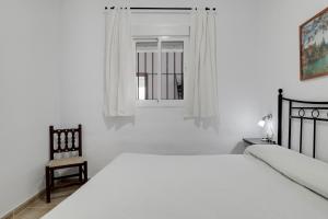 a white bedroom with a bed and a chair at Juani en Conil in Conil de la Frontera