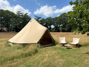 a tent and two chairs in a field at Boutique tent bij Laaken op Zand unieke plek in het groen met luxe bed in Vorden