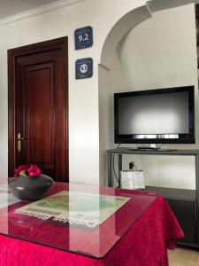 Zimmer mit einem TV und einem Tisch mit einem roten Tuch. in der Unterkunft Casa Rural Cuevas del Sol in Setenil de las Bodegas