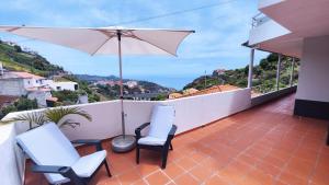 a balcony with two chairs and an umbrella at Quinta do Araújo - GuestHouses in Câmara de Lobos