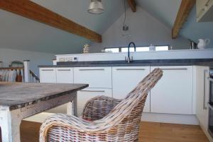 a kitchen with white cabinets and a table with a wicker chair at House 28 in Looe