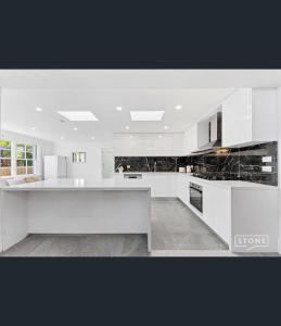 a kitchen with white cabinets and black counter tops at Spacious 5BD Garden House in Hornsby close 2 train in Hornsby