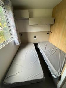 two beds in a small room with a window at Mobil Home Premium Camping Mayotte 5 CLIM TV LV R096 in Biscarrosse