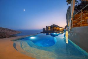 a swimming pool with a view of the ocean at night at Aegean Castle Andros – Adults Only in Agia Eleousa