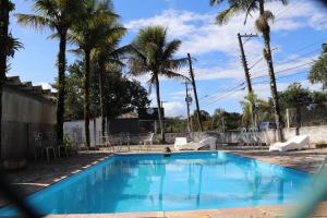 a blue swimming pool with palm trees and chairs at Camping Pousada Ilha do Mel - Frente ao Mar in Boracéia