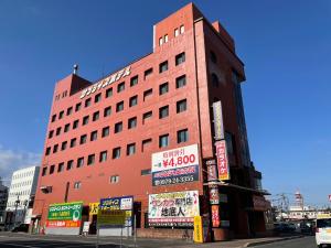 Un edificio alto y rojo con carteles delante. en 中津サンライズホテル, en Nakatsu