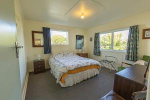 Un dormitorio con una cama y un escritorio y dos ventanas. en Classic Kiwi Bach Southbay, en Kaikoura