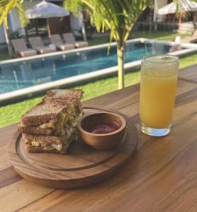 a sandwich and a glass of orange juice on a wooden table at Tropical Almond Villa in Uluwatu