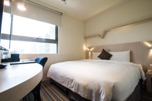 a bedroom with a bed and a desk and a window at Merryday Hotel Banqiao in Taipei