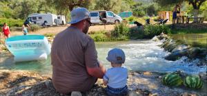 a man and a child sitting next to a river at Camping Parknight in Piqeras