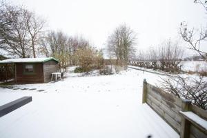 une cour enneigée avec une maison et une clôture dans l'établissement Ferienhaus Deichstern, à Hoddersdeich