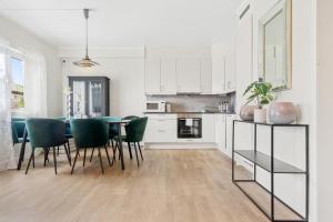 a white kitchen with a table and green chairs at Sentrum Lux Apartment in Vestvågøya