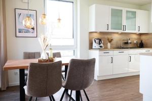 une cuisine avec des armoires blanches et une table et des chaises en bois dans l'établissement BeltBlick 14- Küstenleuchten - Moderne Ferienwohnung direkt am Strand mit Sauna und Garten!, à Fehmarn