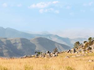 eine Gruppe von Felsen auf einem Feld mit Bergen im Hintergrund in der Unterkunft Mount Sheba Rainforest & Resort Self Catering Cottages in Pilgrimʼs Rest