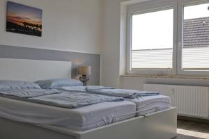 un letto bianco in una stanza con due finestre di Inselblume 58 - Ferienwohnung mit Balkon in Neue Tiefe a Neue Tiefe Fehmarn