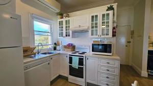 Una cocina con gabinetes blancos, un fregadero y un microondas. en Direct Beachfront Sunrise Apartment - The Coachhouse, en Narrabeen
